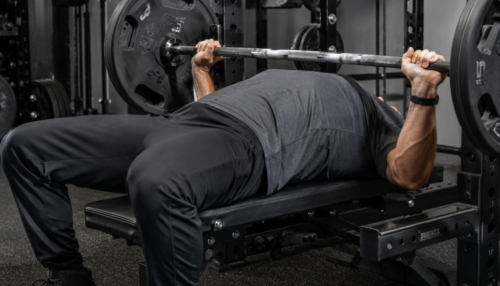 Lifter mid-bench-press viewed from the side in gym