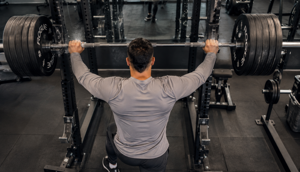 Lifter racking a barbell viewed from behind in gym.