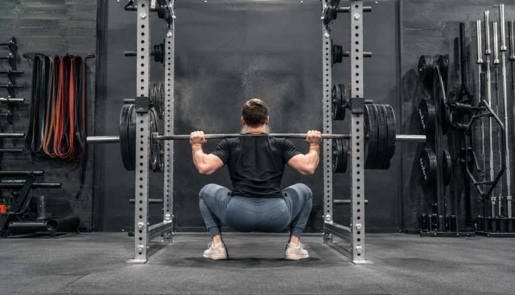 Person performing a deep barbell back squat viewed from behind in gym