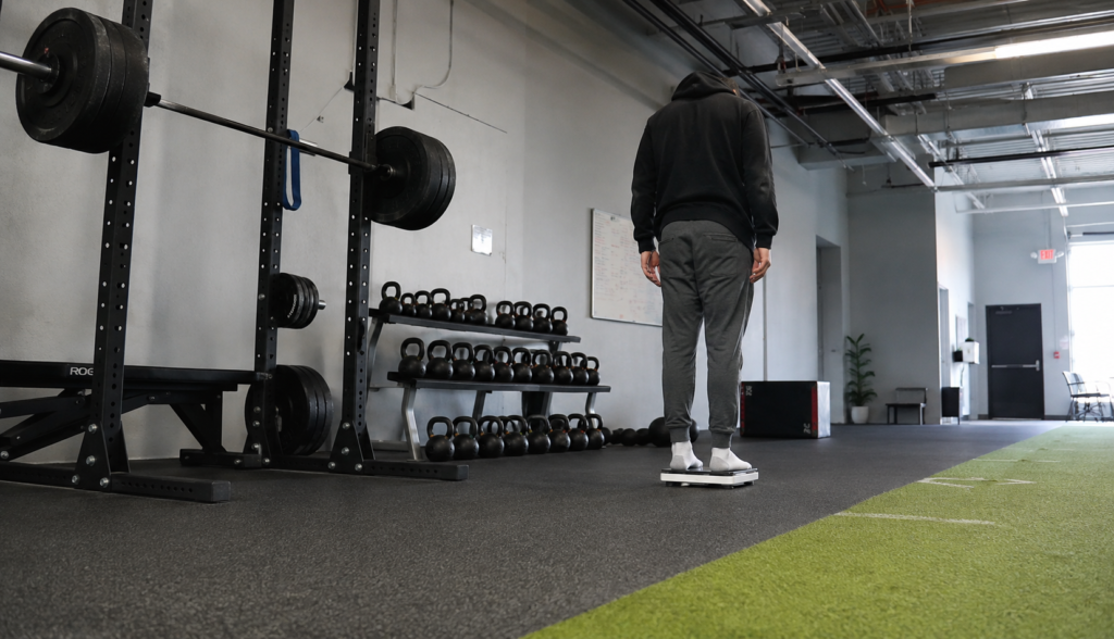 Wide gym shot with squat rack and person stepping onto scale
