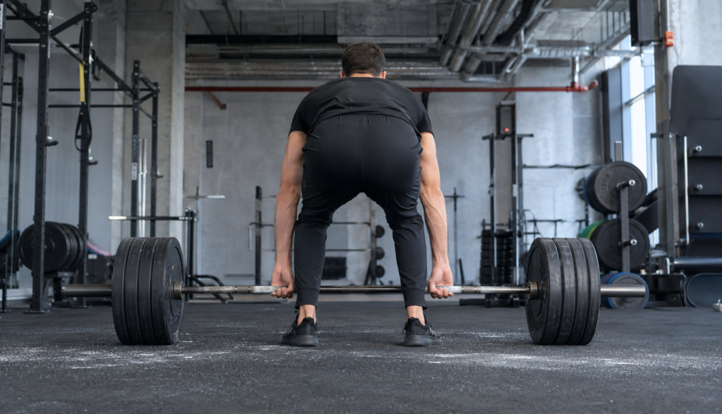 Lifter deadlifting a barbell from behind on rubber gym flooring