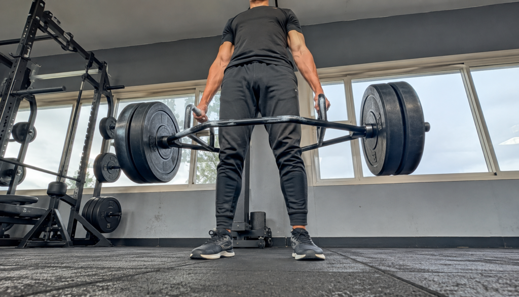 Lifter at lockout on a trap bar deadlift, shot from a low floor angle.
