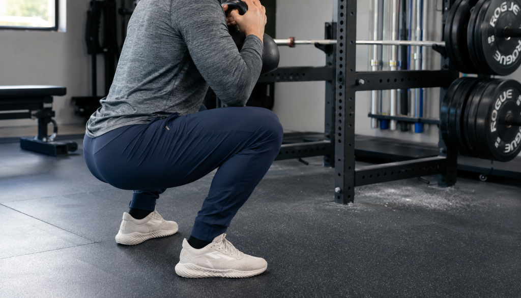 Athlete performing a three-quarter angle kettlebell goblet squat, face not visible
