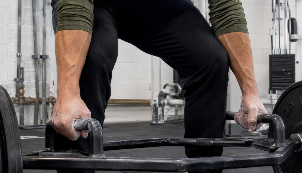 Close-up of chalked hands gripping a trap bar mid-lift