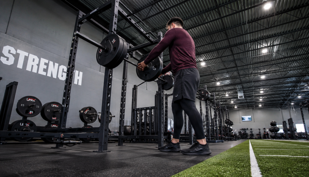 Wide gym shot of a lifter loading plates from a low floor angle