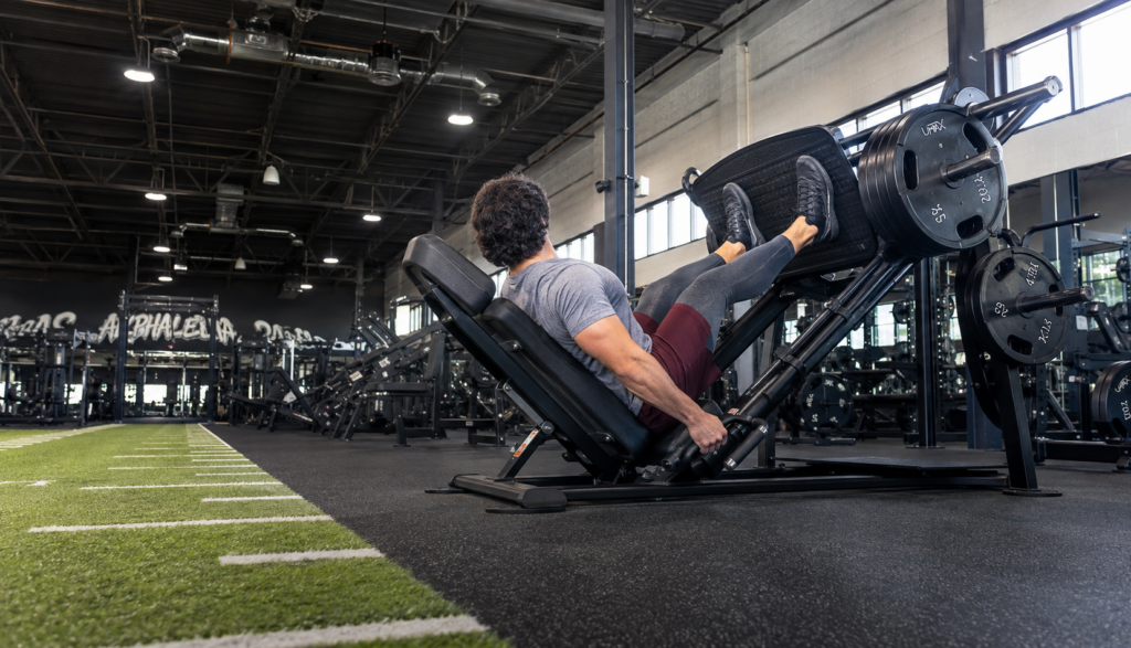 Lifter at lockout on a leg press machine in a full gym setting