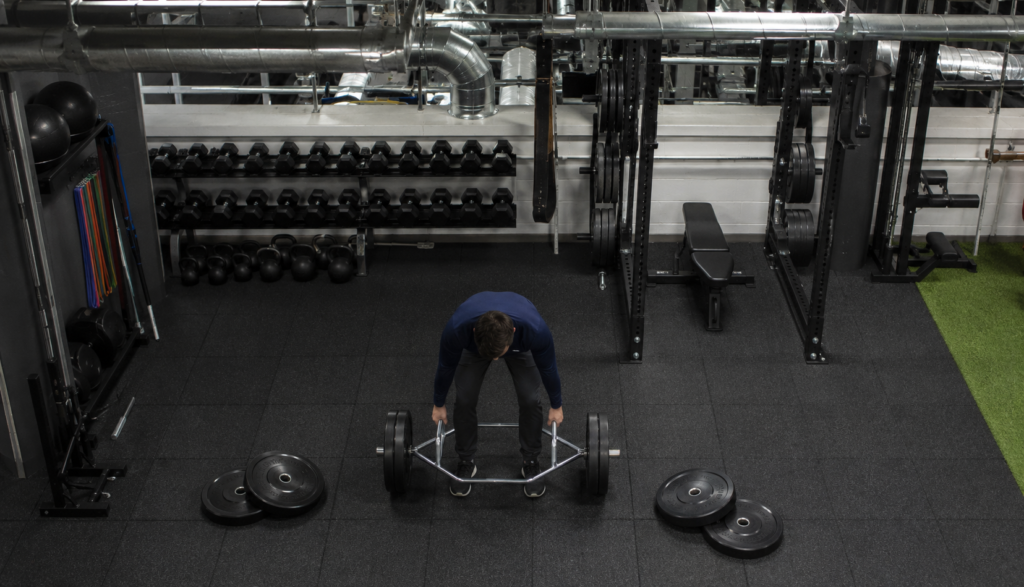 Lifter loading a trap bar with weight plates in a gym