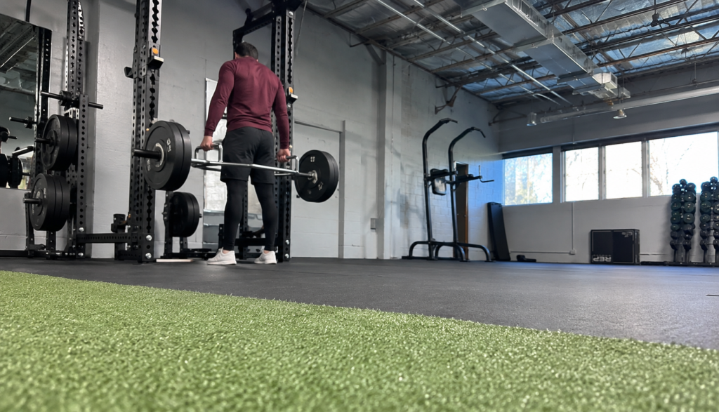 Wide gym shot of a lifter racking a trap bar from a low angle.