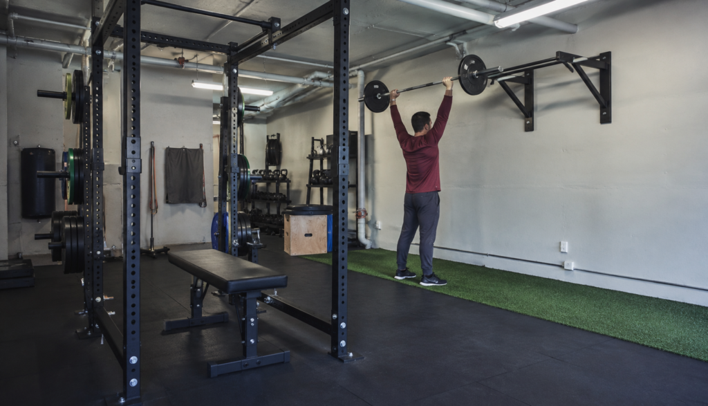 Wide view of a home gym setup with a lifter racking an overhead press