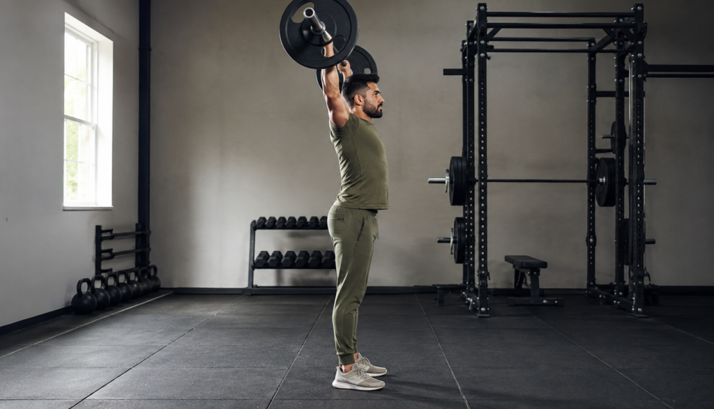 Lifter performing barbell overhead press from side profile angle in gym