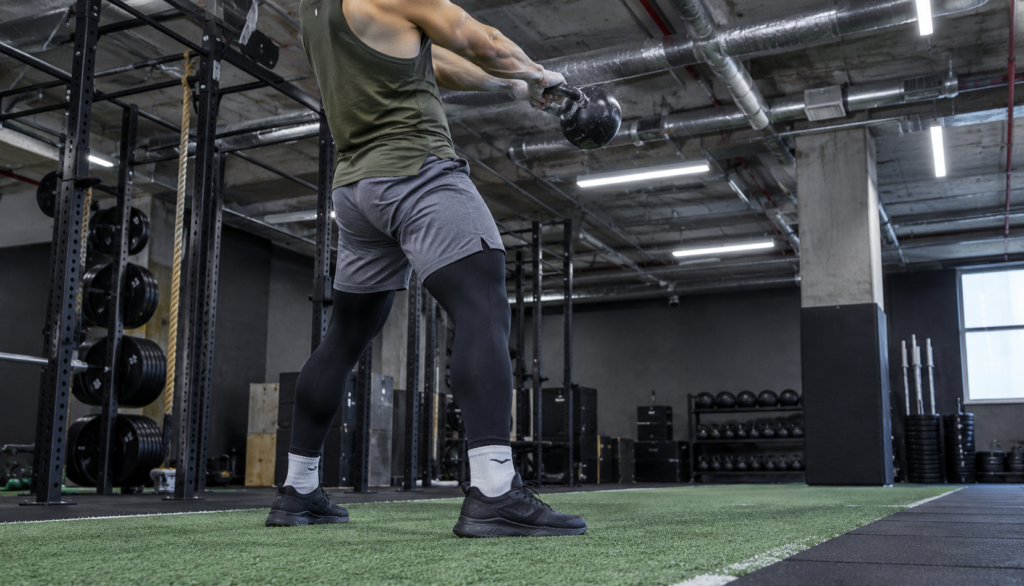 Lifter mid-swing with kettlebell on gym turf strip