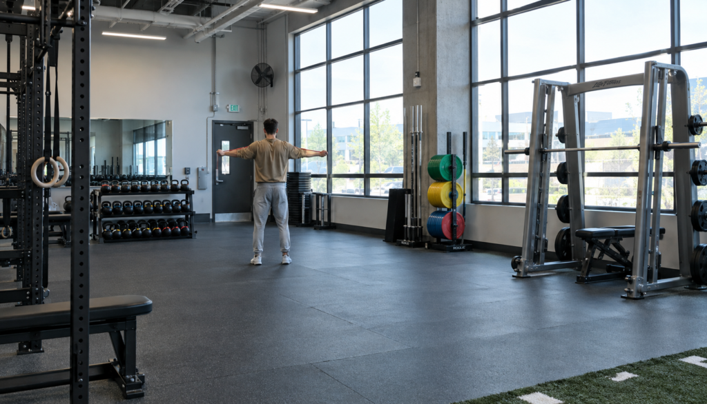 Wide view of a lifter doing band pull-aparts on an open gym floor